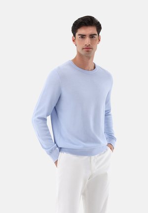 Light blue knit sweater with a round neckline, ribbed cuffs, and hem. Paired with white trousers, displaying a smooth, soft texture.