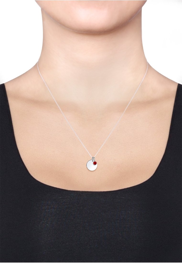 Collier en argent avec un pendentif circulaire et un accent rouge. Le pendentif a une surface lisse et est suspendu à une chaîne fine.