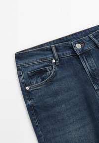 Jeans en denim bleu foncé avec un léger dégradé, présentant un design à cinq poches, un bouton en métal et des coutures contrastées.