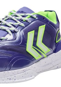 Lila träningssko med en texturerad ovandel, neongröna accenter och reflexdetaljer. Har en vitprickig sula och mönstrade skosnören.