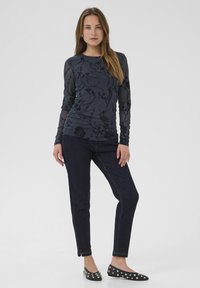 Langsleeve marineblauw top met bloemenpatroon, gecombineerd met donkere jeans en zwarte flats met zilveren studs. Glad materiaal en aansluitend ontwerp.