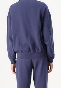 Marineblauwe sweatshirt van zachte stof, met een geribbelde zoom en manchetten, en verlaagde schoudernaad voor een ontspannen pasvorm.