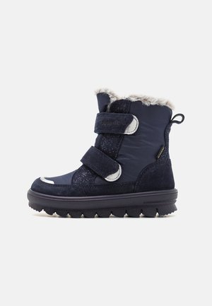 Dunkelblaue Winterstiefel mit Kunstfellfutter, aus Wildleder und Textil, mit Klettverschlüssen und einer strukturierten Gummisohle, die über kreisförmige Griffe verfügt.