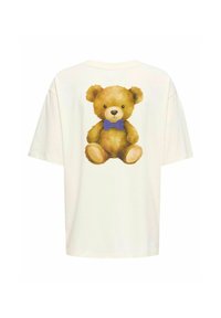T-shirt surdimensionné couleur crème avec un graphique de nounours portant un nœud papillon bleu dans le dos. Texture douce et coupe décontractée.