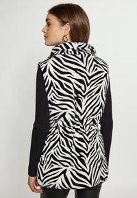 Zebra print vest in zwart-wit met een kraag, elastische taille en ribgebreide zwarte mouwen. Glad stof, puffy textuur en twee voorkeizen.