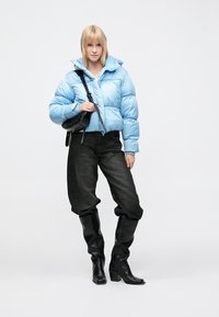 Ljusblå vadderad jacka med hög krage, svart axelväska, svarta högklackade stövlar och löst sittande svarta jeans. Mjuk textur överallt.