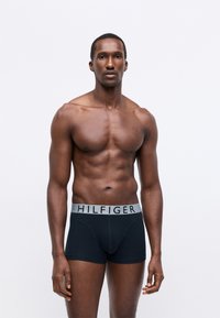Black boxer briefs with a grey waistband featuring the "HILFIGER" logo, made of a smooth, stretchy material, fitting snugly.