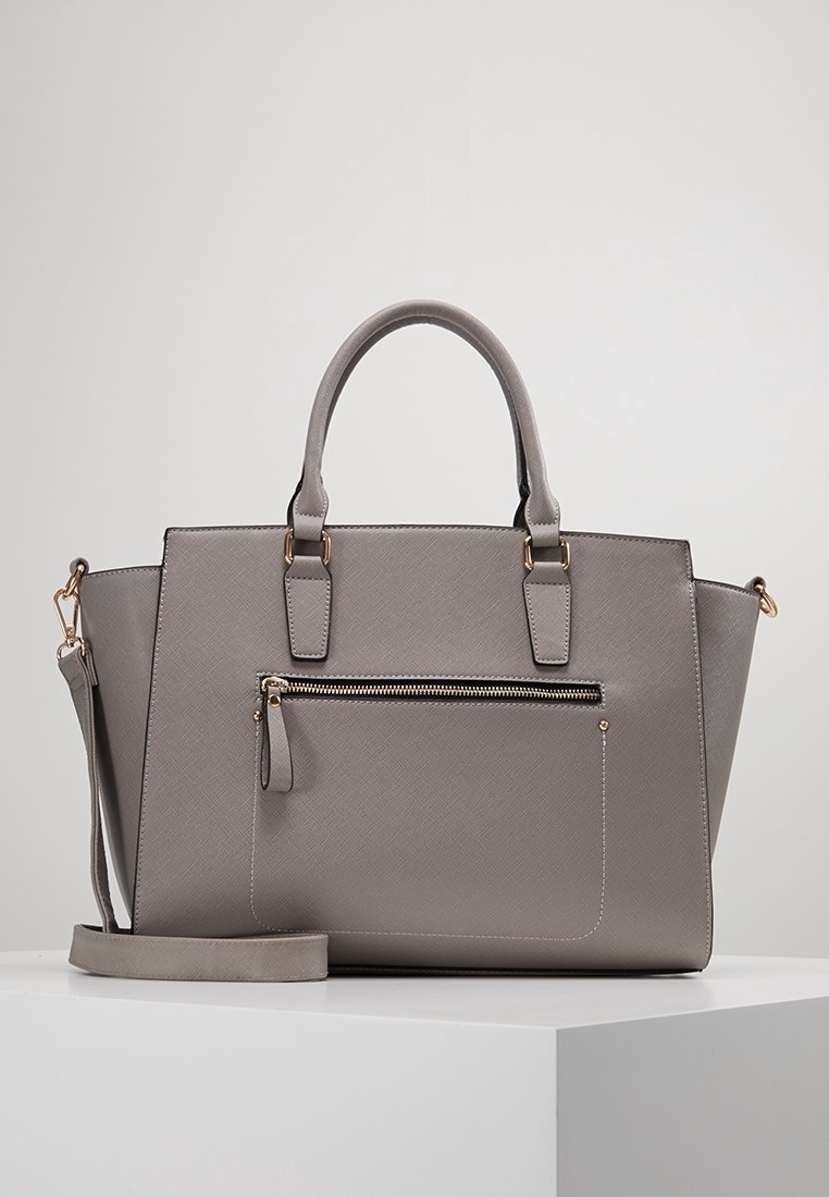 Sac à main en cuir gris texturé avec deux poignées, une poche frontale zippée et une bandoulière amovible sur une surface blanche.