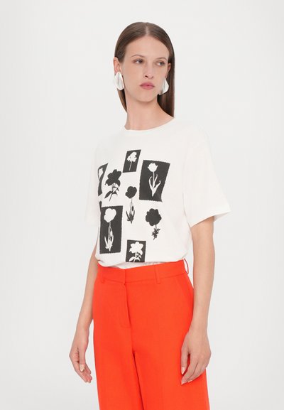 Hvid bomulds T-shirt med et sort blomstermotiv i rektangulære designs. Stylet med lyse orange skræddersyede bukser.