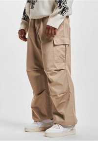 Pantaloni cargo bej cu buzunare laterale, croială lejeră și talie ajustabilă. Asortați cu adidași albi pentru un aspect relaxat.