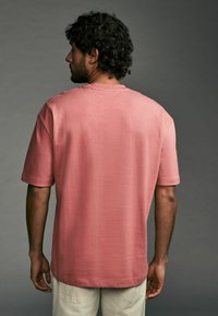 Kurzärmliges T-Shirt in zartrosa aus weichem Stoff, mit lockerer Passform und rundem Halsausschnitt. Sichtbare Nähte an den Schultern.