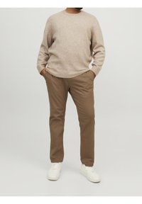 Maglione beige chiaro lavorato a maglia con orlo a coste abbinato a pantaloni color tan e sneaker bianche, caratterizzato da una texture liscia e taglio a gamba dritta.