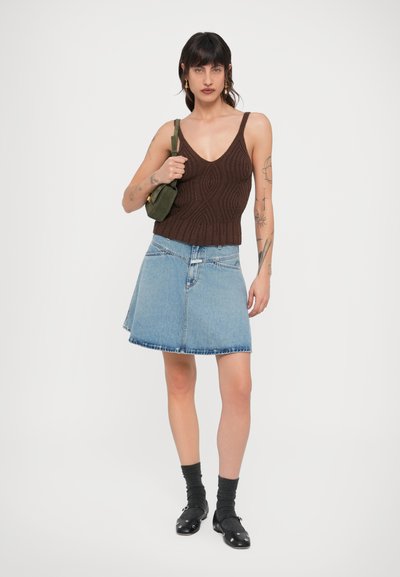 Καφέ πλεκτό αμάνικο τοπ με V-λαιμόκοψη, συνδυασμένο με φούστα A-line από γαλάζιο τζιν. Αξεσουάρ περιλαμβάνουν μικρή πράσινη τσάντα και μαύρα παπούτσια.