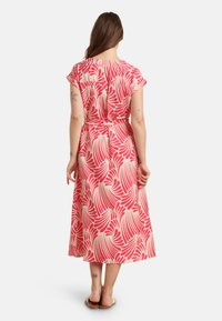 Rotes und cremefarbenes Midikleid mit Blattdruck, kurzen Ärmeln, tailliertem Schnitt und fließender Silhouette. Getragen mit flachen Sandalen.