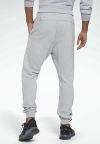 Graue Jogginghosen mit strukturierter Oberfläche, elastischem Bund, gerippten Bündchen und seitlichen Taschen, kombiniert mit schwarzen Sportschuhen.