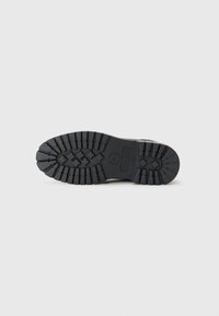 Suela de bota de goma negra con un patrón de tracción robusto, que presenta profundas ranuras y un emblema circular. Diseño plano y resistente para una buena tracción.