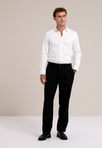 Camicia bianca a maniche lunghe e pantaloni neri da abito. La camicia presenta un colletto classico e un design aderente. I pantaloni hanno un taglio dritto con tasche frontali.