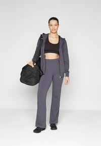 Siva jakna s kapuljačom, crni crop top i siva wide-leg hlače. Crna torba s mrežastim detaljima. Crna obuća. Jednostavan, sportski dizajn.
