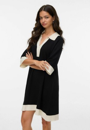 Black dress with a V-neck, featuring a cream collar and cuffs. The fabric appears soft with a relaxed fit and a mid-thigh length.