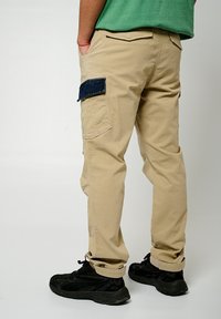 Beige cargobroek met een donkerblauwe zijzak, met een losse pasvorm, opgerolde zoom en een soepele katoenstructuur. Draagt met zwarte sneakers.