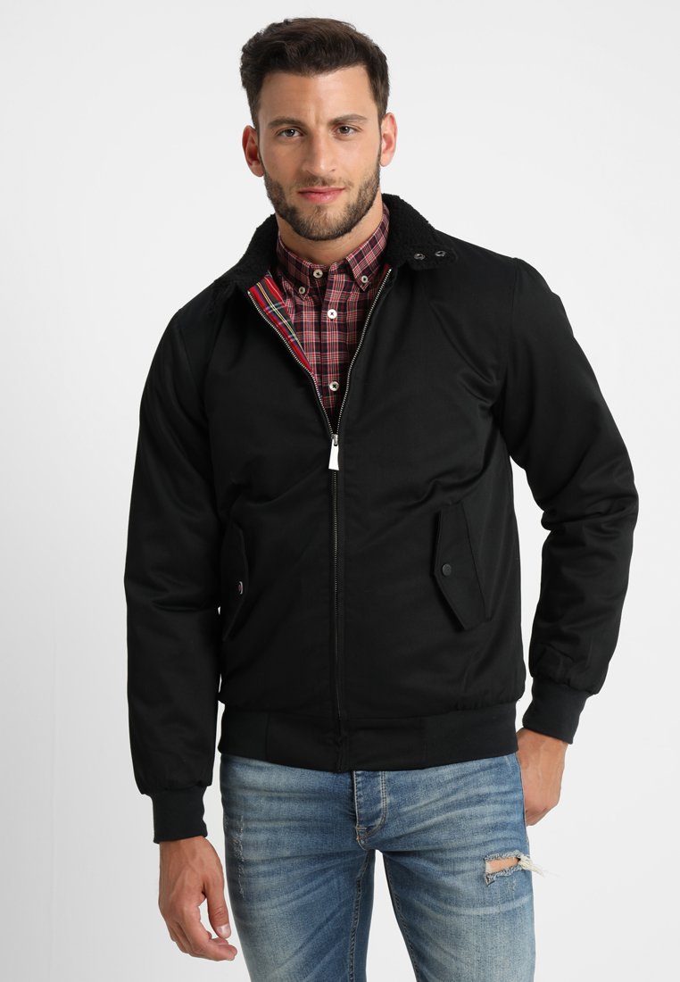 Veste bomber noire avec fermeture éclair à l'avant, col en peluche et poches latérales. Portée sur une chemise à carreaux rouge, en tissu texturé et au design ajusté.