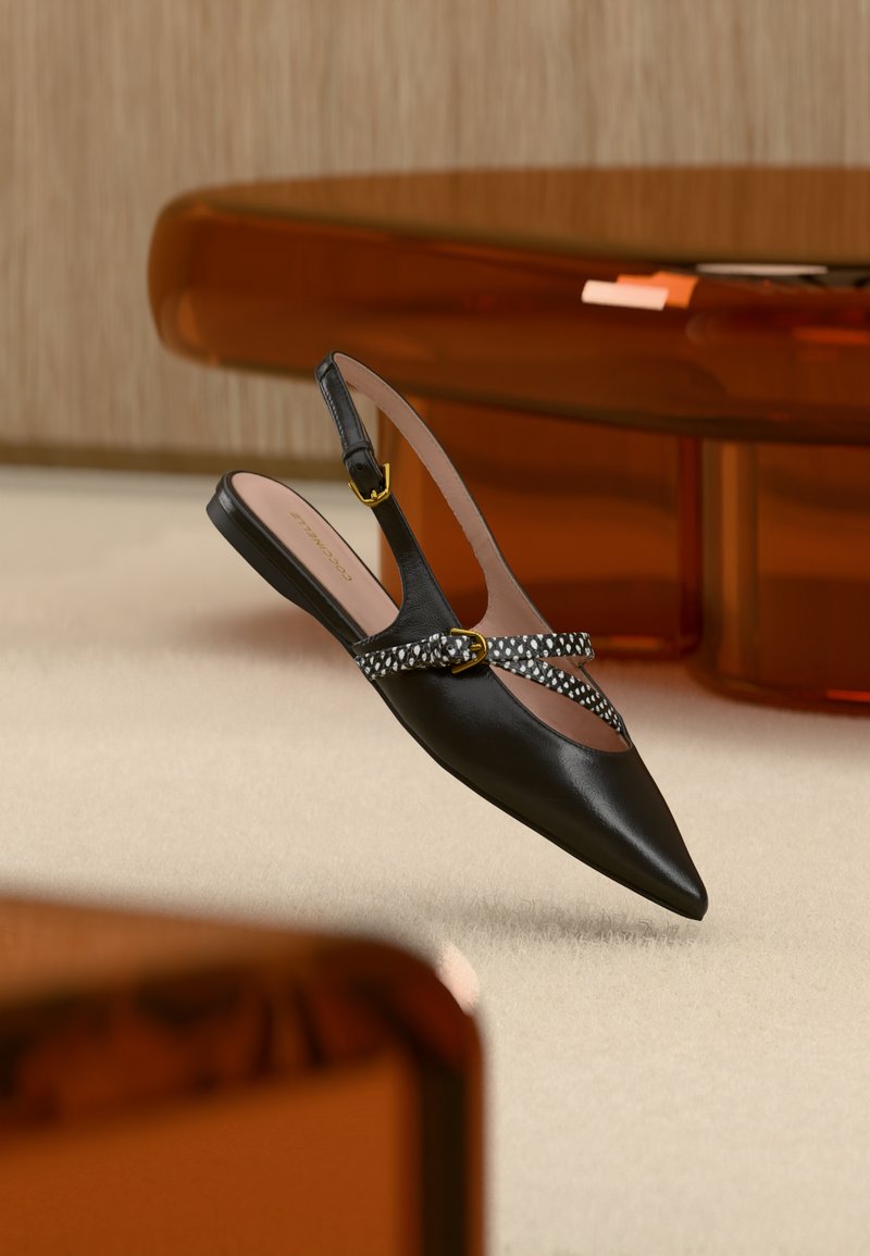 Μαύρη παιδική μπαλαρίνα με μυτερή μύτη, λουράκια με μοτίβο λεοπάρ και χρυσά αγκράφες, τοποθετημένη πάνω σε μπεζ χαλί δίπλα σε καφέ διάφανα έπιπλα.