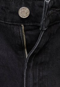 Gros plan sur un tissu en denim noir avec un bouton en métal et une fermeture éclair argentée partiellement visible sur un jean.