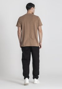 Korte mouw, geribbelde bruine shirt gecombineerd met zwarte broek en witte sneakers, gezien vanaf de achterkant, met nadruk op textuur en snit.