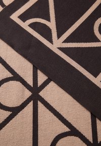 Two overlapping knitted fabrics with beige and dark brown geometric patterns featuring circles and diagonal lines.