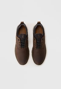 Une paire de chaussures décontractées en cuir marron avec des lacets noirs et des semelles beiges, vue de dessus sur un fond blanc.