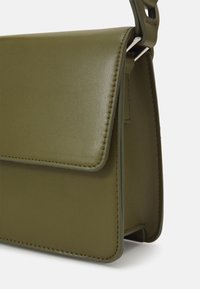 Kompaktowa oliwkowo-zielona skórzana torebka z klapką i pojedynczym górnym uchwytem, przedstawiona z boku.