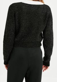 Pull noir en tricot avec une texture côtelée, doté d'un large col blanc. Design court et coupe légèrement ample, mettant en valeur un effet scintillant.