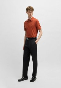 Orange polo skjorta med korta ärmar, svarta skräddarsydda byxor och svarta skor. Slät tyg, figursydd design och diskret logotypdetalj på bröstet.