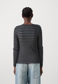 Långärmad, ribbad topp med ett mörkgrått och svart horisontellt randmönster, kombinerat med ljusblå, löst sittande denimjeans.