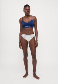 Jūras zila bralette ar "POLO" logo, apvienots ar baltām biksītem ar mežģīņu apdari, ar gludu tekstūru un pieguļošu dizainu.