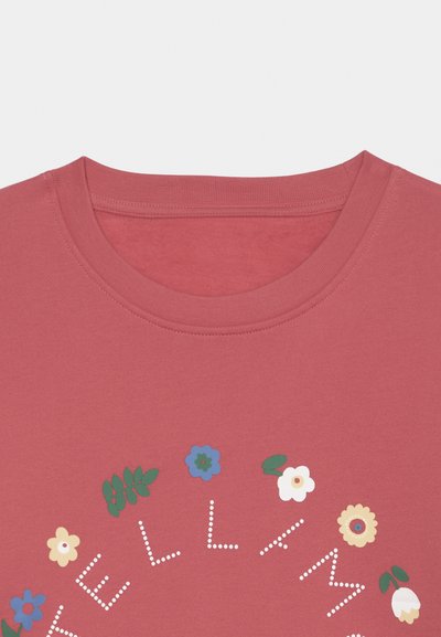 Κόκκινη μπλούζα με στρογγυλό floral σχέδιο και λευκό κείμενο με τελείες, εν μέρει ορατό στο στήθος.
