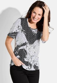 Zwart-wit T-shirt met korte mouwen, versierd met stippen en bloemmotieven, met een ronde halslijn en een relaxed fit. Gemaakt van lichte stof.