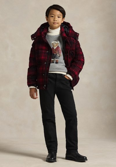 Μπουφάν με κόκκινο και μαύρο καρό σχέδιο και κουκούλα, φορεμένο πάνω από γκρι πουλόβερ με γραφικό σχέδιο. Μαύρο παντελόνι και μαύρες μποτάκια αστραγάλου ολοκληρώνουν το σύνολο.