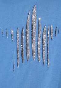 Tejido azul con un recorte en forma de estrella relleno de lentejuelas plateadas en formas alargadas y puntiagudas, que añaden un detalle texturizado al diseño.