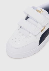 Witte sneaker met marineblauwe accenten, gemaakt van synthetisch materiaal. Beschikt over twee klittenbandsluitingen, geperforeerde neus voor ventilatie en een rubberen zool.