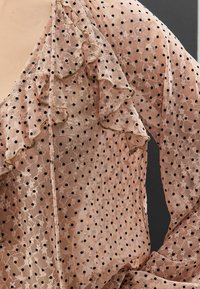 Blouse rose pâle en tissu transparent avec un motif à pois, des bords volantés et de délicates accents floraux.