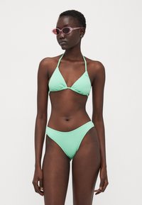 Mentazöld bikini szett, textúrált háromszög melltartóval és magas derekú alsó résszel. A modellen rózsaszín napszemüveg van, átlátszó kerettel.