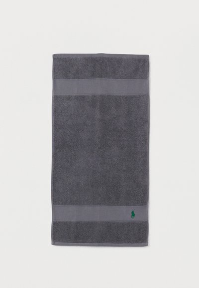 Σκούρο γκρι πετσέτα με υφασμάτινες ταινίες στην κορυφή και στο κάτω μέρος, με μικρό πράσινο κεντημένο λογότυπο κοντά στην κάτω άκρη.