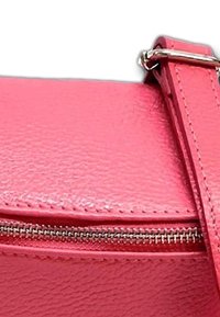Roze gestructureerde leren tas met een zilveren ritsdetail. De schouderriem is bevestigd met metalen hardware, wat toont dat de stiknaden versterkt zijn.