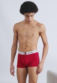Κόκκινα ανδρικά εσώρουχα boxer από βαμβάκι με λευκή ελαστική ζώνη μέσης που φέρει το λογότυπο 'TOMMY HILFIGER' και διακοσμητικό σχέδιο με ρίγες.