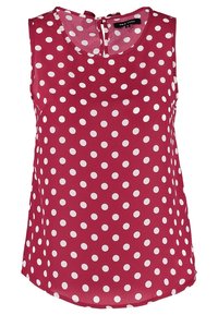 Blouse rouge sans manches avec un col rond et des pois blancs, avec une fermeture à boutons dans le dos au niveau du col.