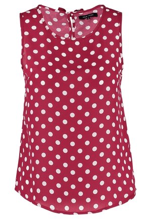Personne portant une veste en jean noire sur une chemise rouge à pois, un jean clair déchiré retroussé aux poignets, et des chaussures blanches à lacets.