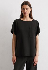Schwarzes Kurzarmoberteil aus weichem Material, mit Rundhalsausschnitt und einer Brusttasche. Einfaches, locker sitzendes Design mit minimalen Details.