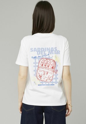T-shirt en coton blanc avec un graphique coloré de sardines en conserve, accompagné de texte en bleu et rouge, le tout accentué par un motif de grille.