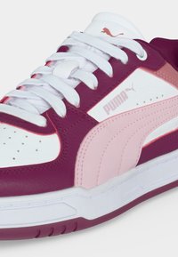 Κοντινή λήψη από ένα μαρόν και ροζ sneaker Puma με λευκά κορδόνια, που δείχνει το λογότυπο στην πλευρά και τη γλώσσα και διατρήσεις στο μπροστινό μέρος.